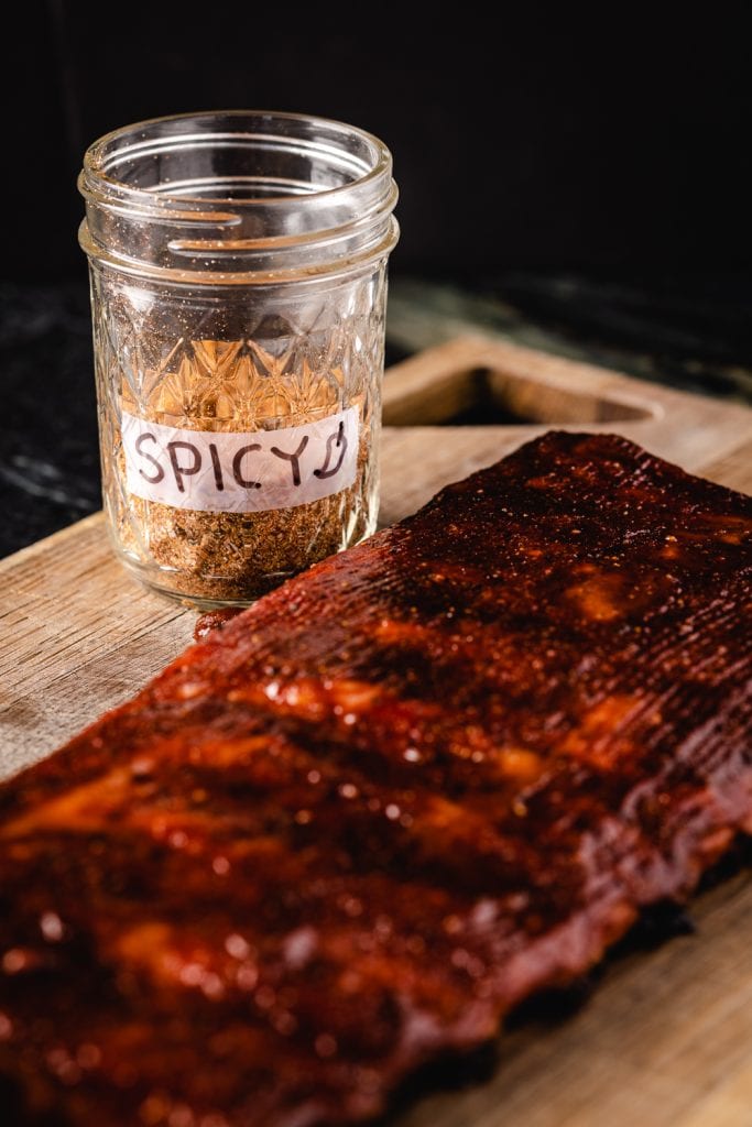 Jar of hot sweet rub next to a rack of ribs.