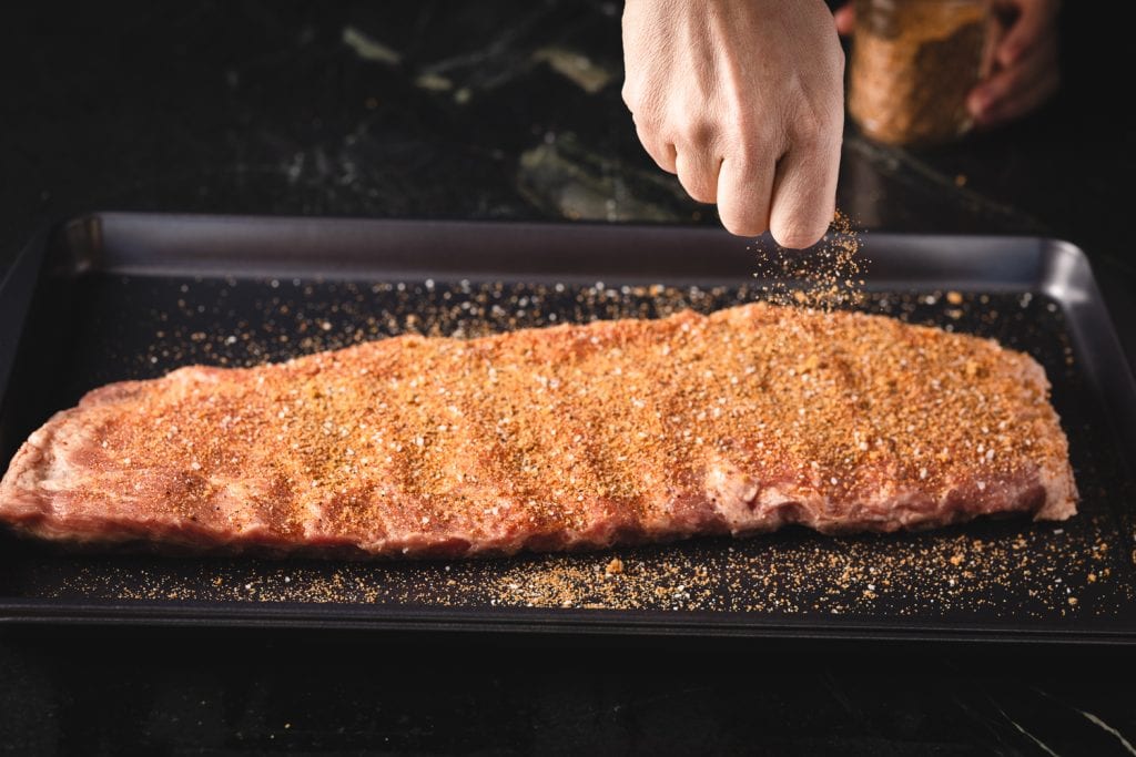 Hot sweet rub being sprinkled on a rack of ribs.