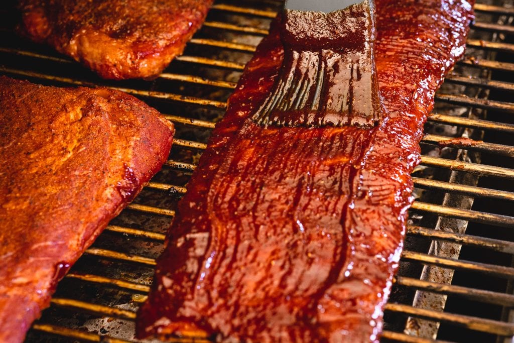 BBQ sauce being brushed on a rack of St. Louis ribs.