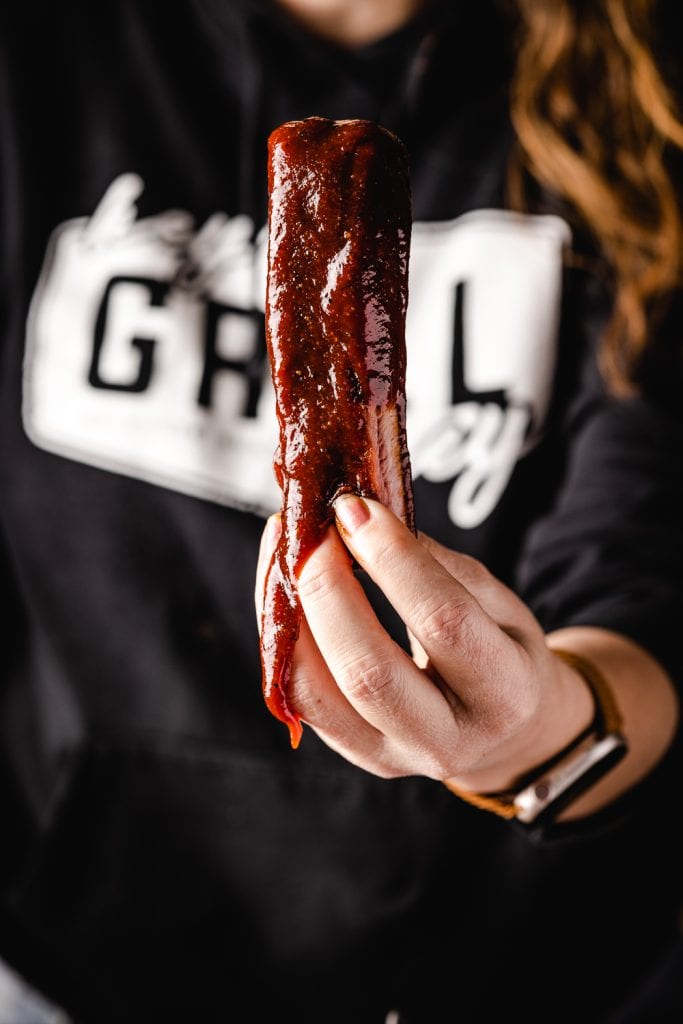 Susie holding a rib covered in sauce.