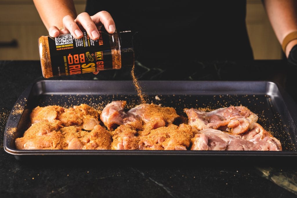 Chicken thighs being seasoned with Hey Grill Hey Sweet Rub.