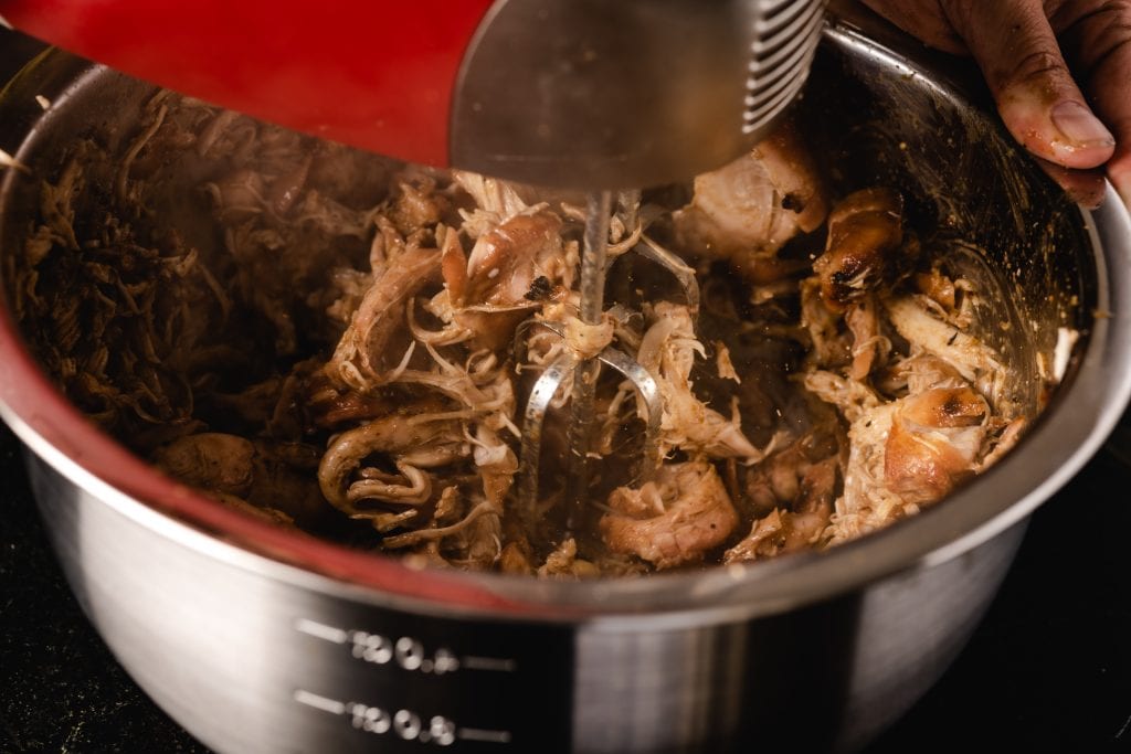 Smoked chicken thighs being shredded by a hand mixer.