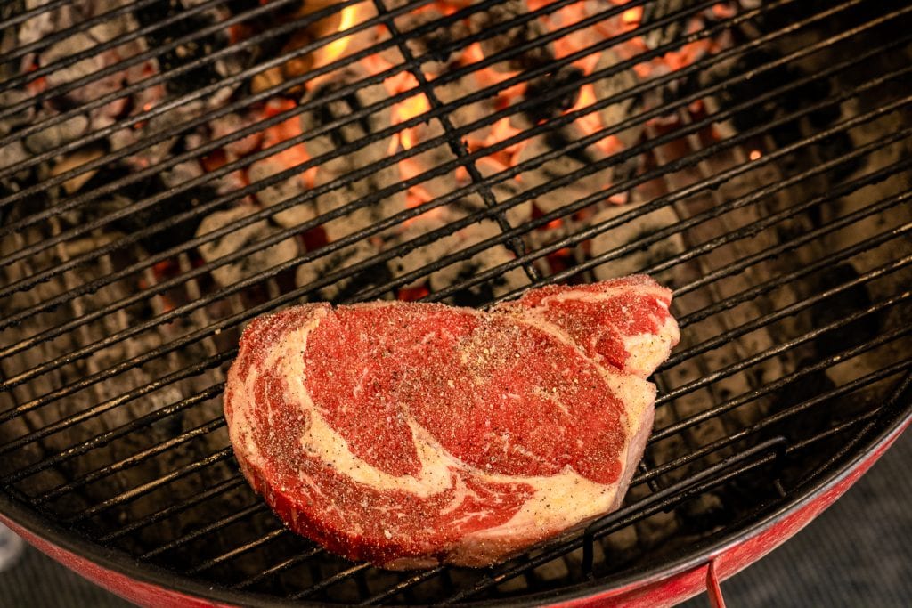 Ribeye steak over indirect heat side of a charcoal grill.