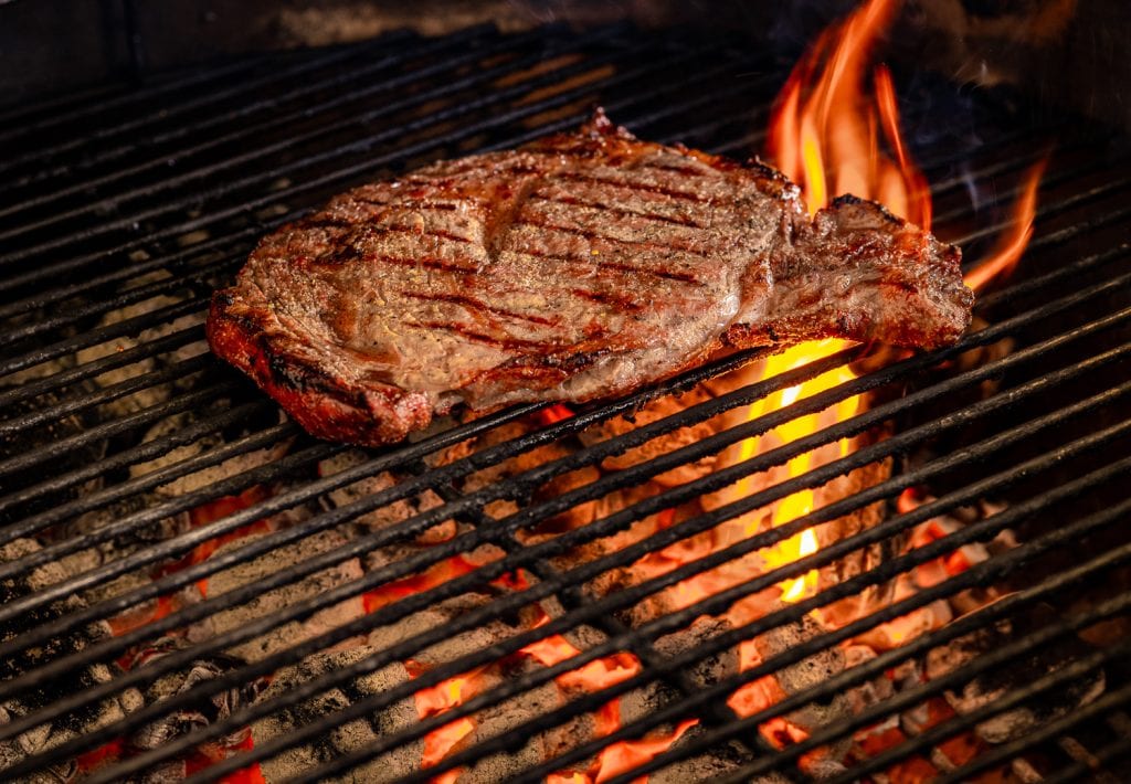 Seasoned ribeye steak over direct heat on a charcoal grill.