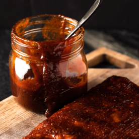 Spicy BBQ sauce in a jar next to a rack of ribs.