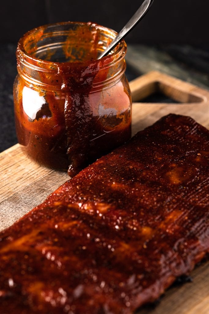Spicy BBQ sauce in a jar next to a rack of ribs.