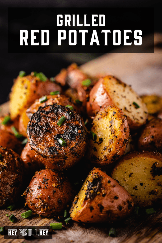 Pile of grilled red potatoes on a cutting board with text overlay - Grilled Red Potatoes.