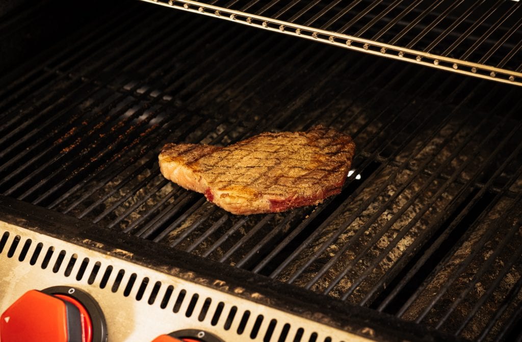 Seasoned steak on a gas grill.