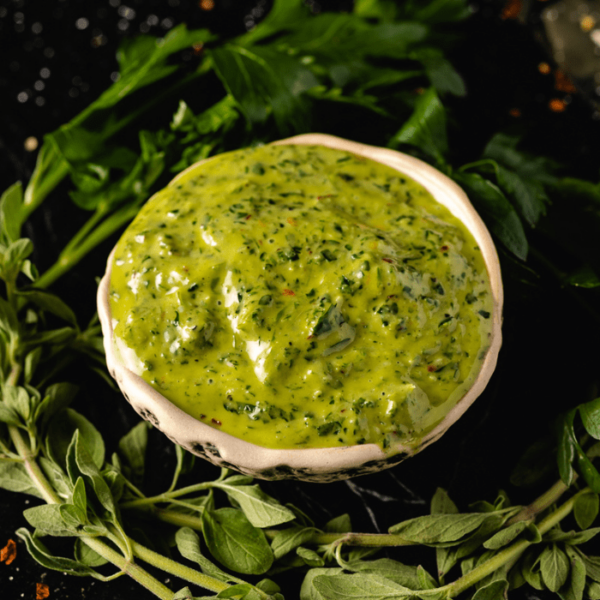 Bowl of chimichurri surrounded by herbs.