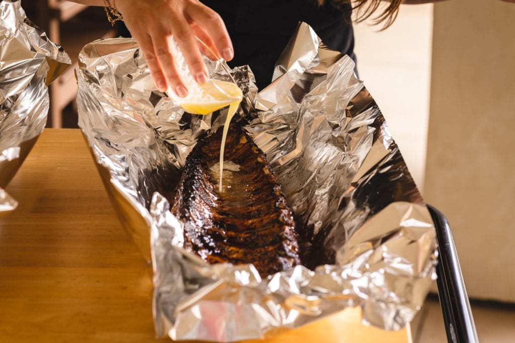 Melted butter being poured on top of a rack of baby back ribs in foil.