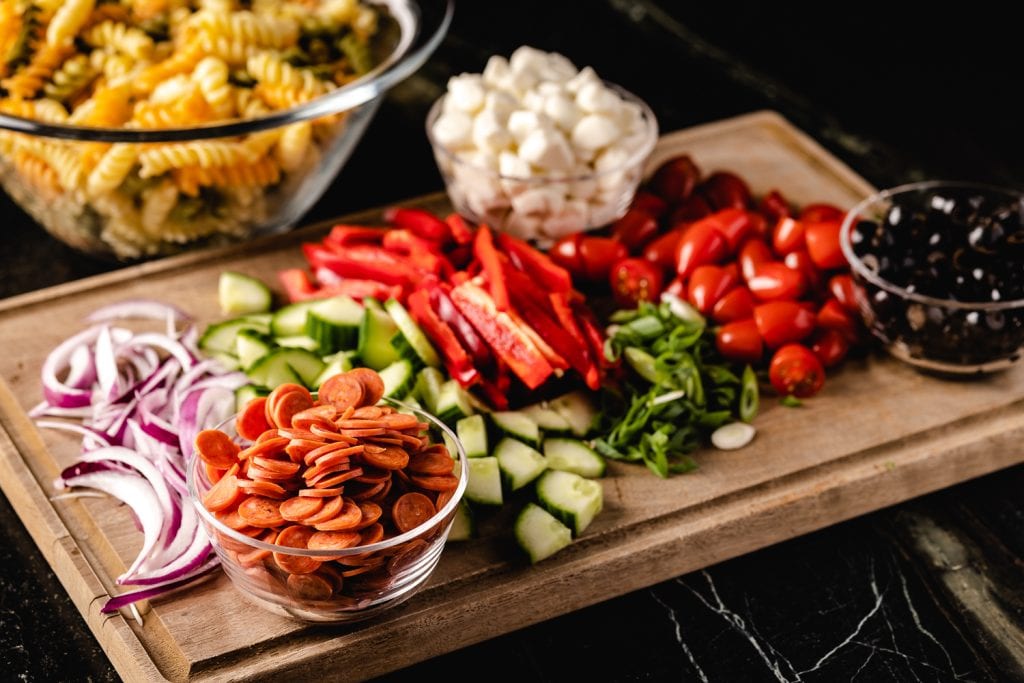 Ingredients for pasta salad arranged on a wooden cutting board.