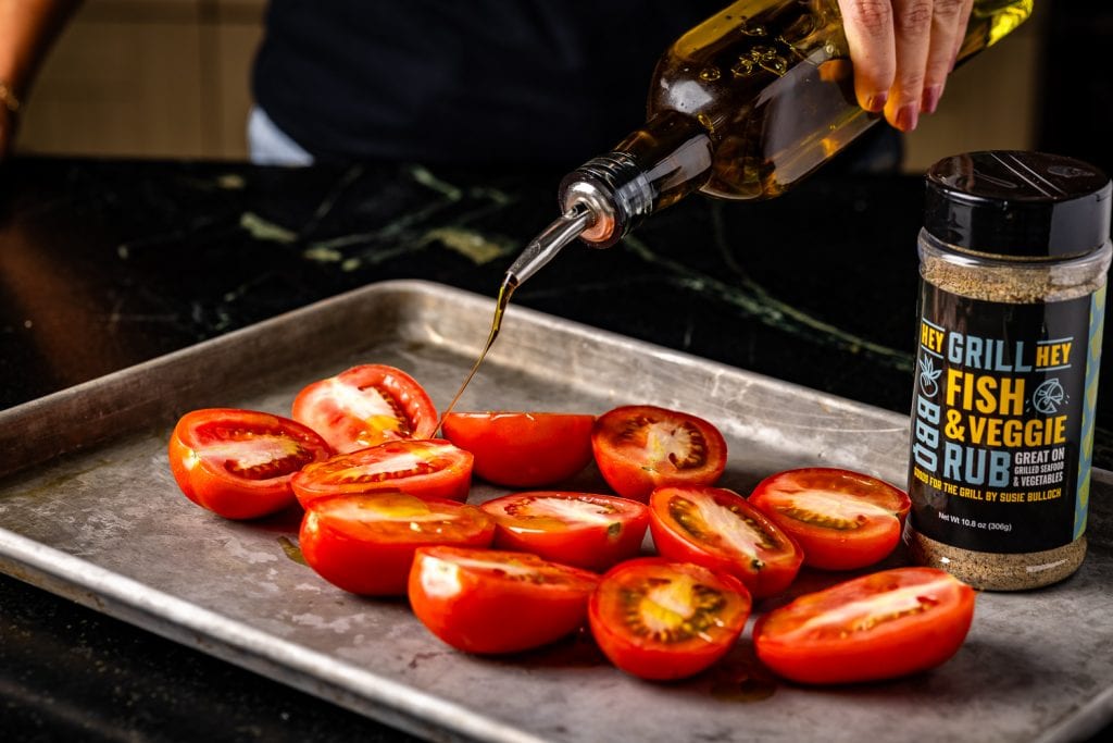 Sliced roma tomatoes being drizzled with olive oil.