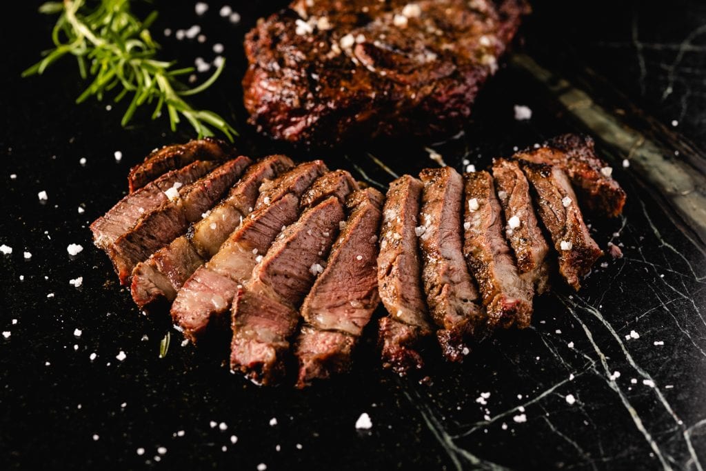 Reverse sear ribeye steak sliced on a serving board.