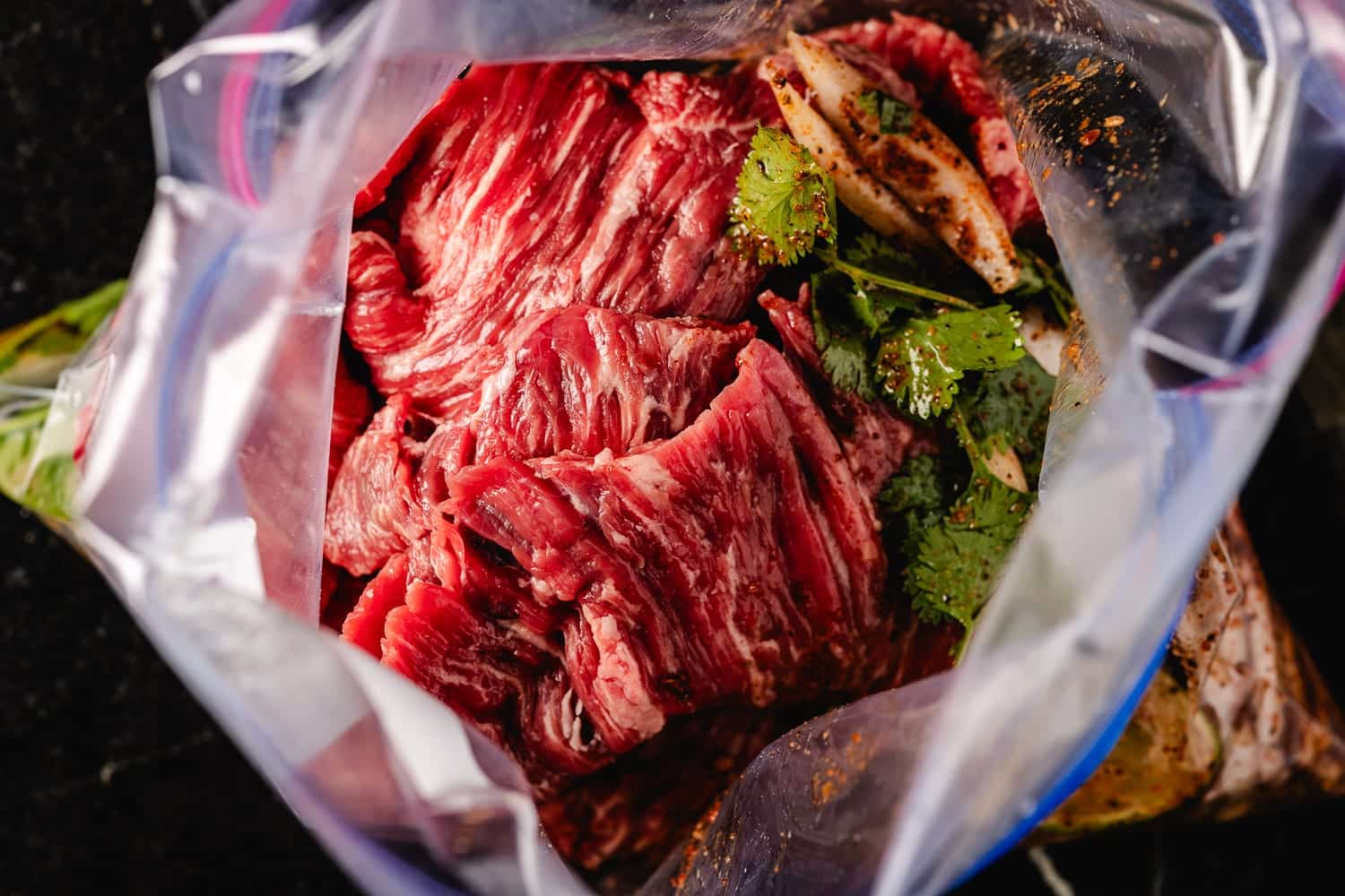 Raw skirt steak in a zip top bag with cilantro and onions.