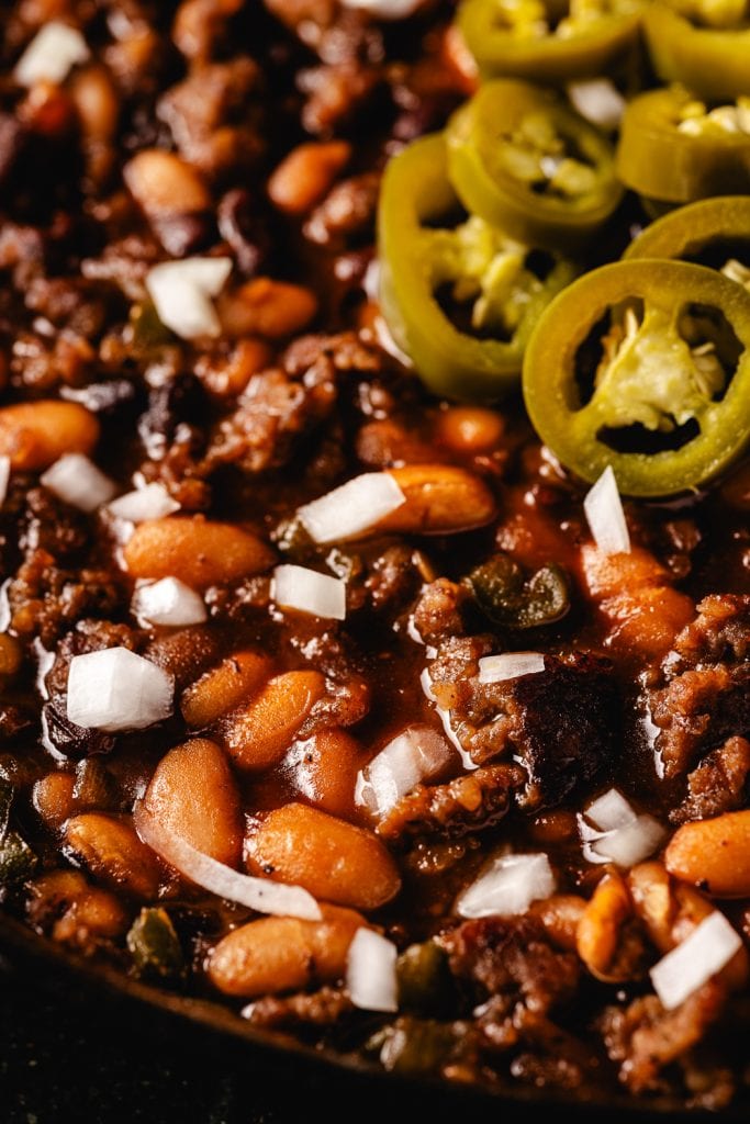 Close up image of cooked pit beans topped with chopped onion and jalapeno