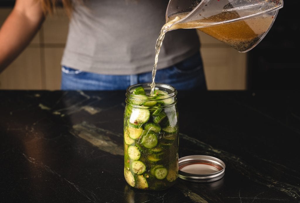 Pickling brine being poured into a glass mason jar full of sliced pickles.