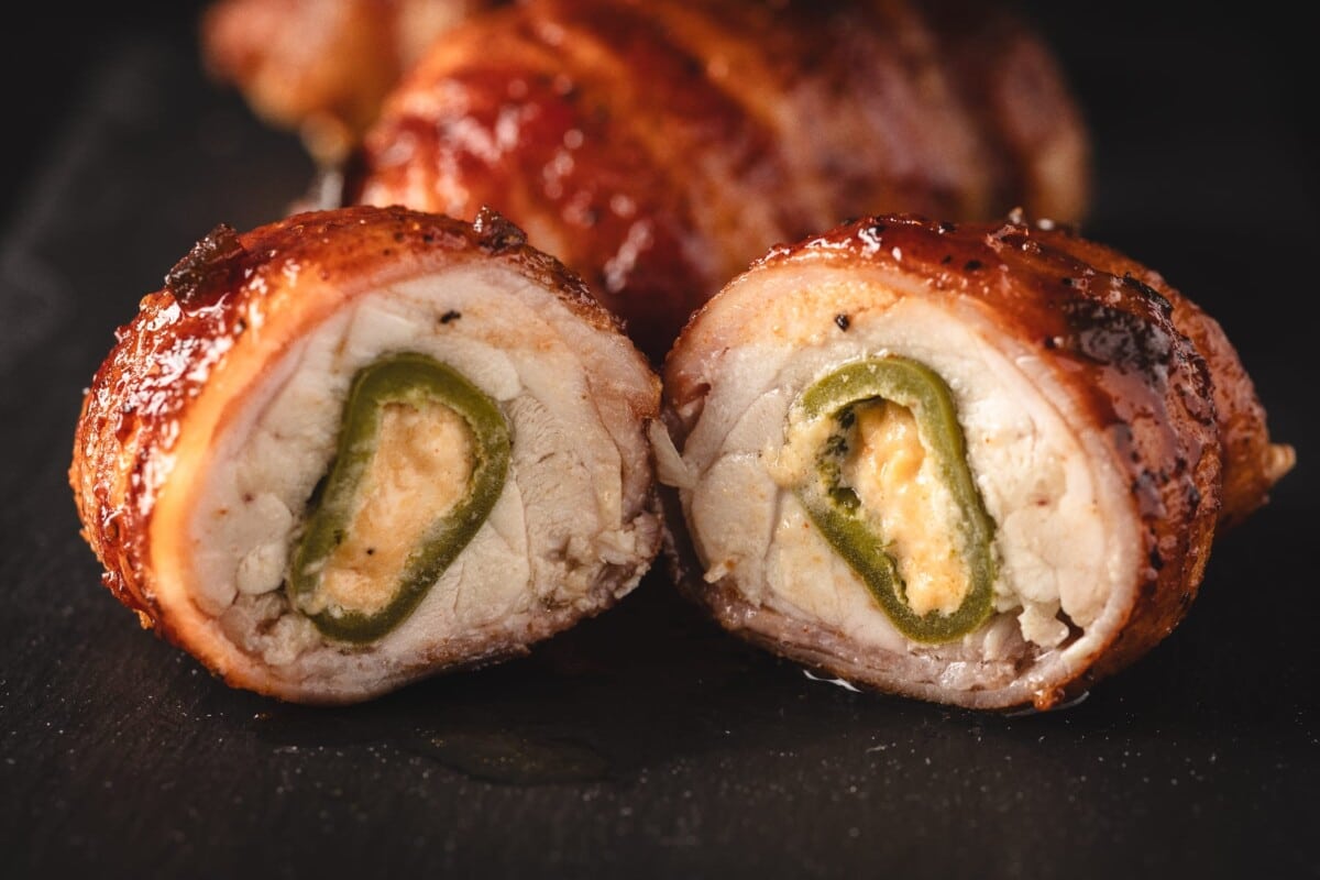 Bacon jalapeño popper chicken bomb sliced in half on cutting board.