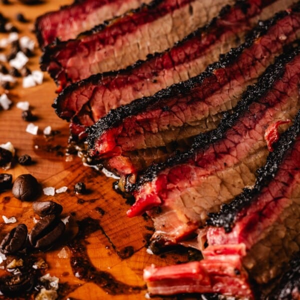 Coffee rubbed brisket slices on cutting board with coffee beans and salt flecks.