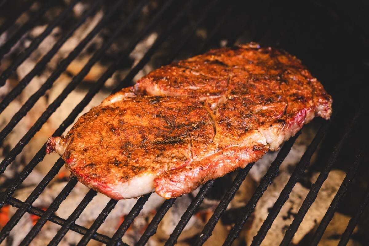 A seasoned steak on the grates of a grill,