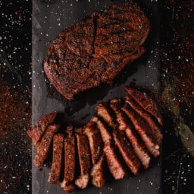 Sliced and whole coffee rubbed steaks on black cutting board.