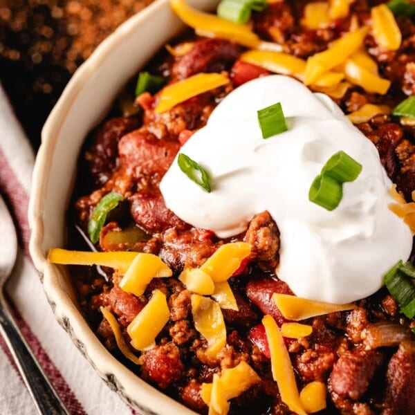 Chili in white bowl with sour cream and shredded cheese.