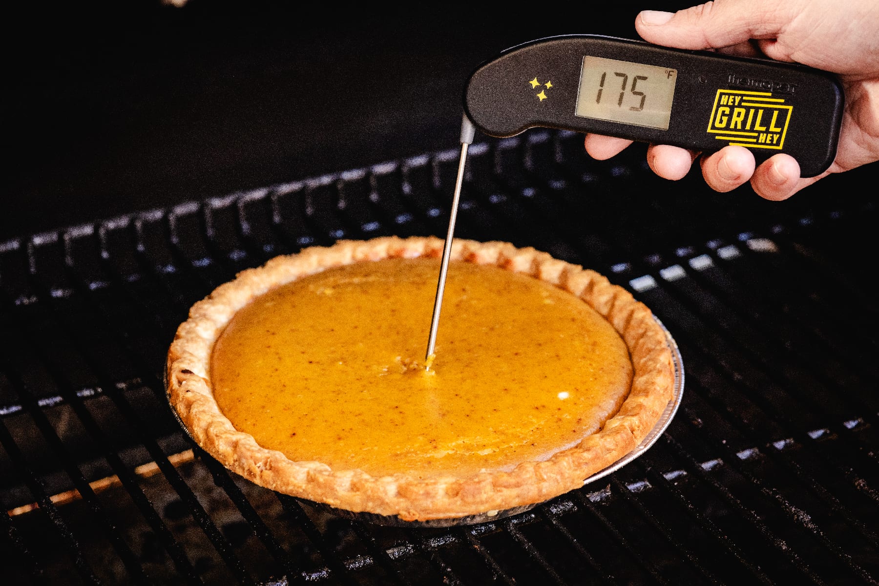 Thermometer taking internal temperature of pumpkin pie on grill reading 175 degrees F.