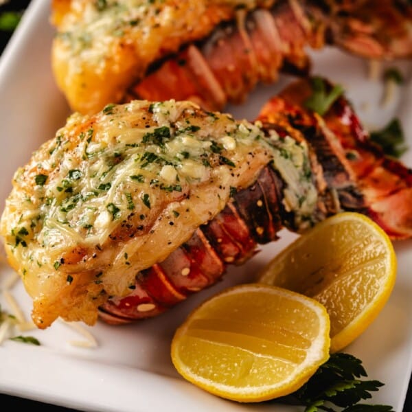 Smoked lobster tails on white plate with lemon wedges.