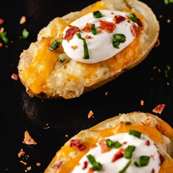 Twice baked potatoes with toppings on black cutting board.