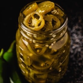Jalapeño slices in mason jar next to whole peppers.