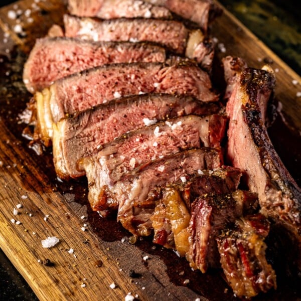 Sliced tomahawk steak with salt and pepper on cutting board.