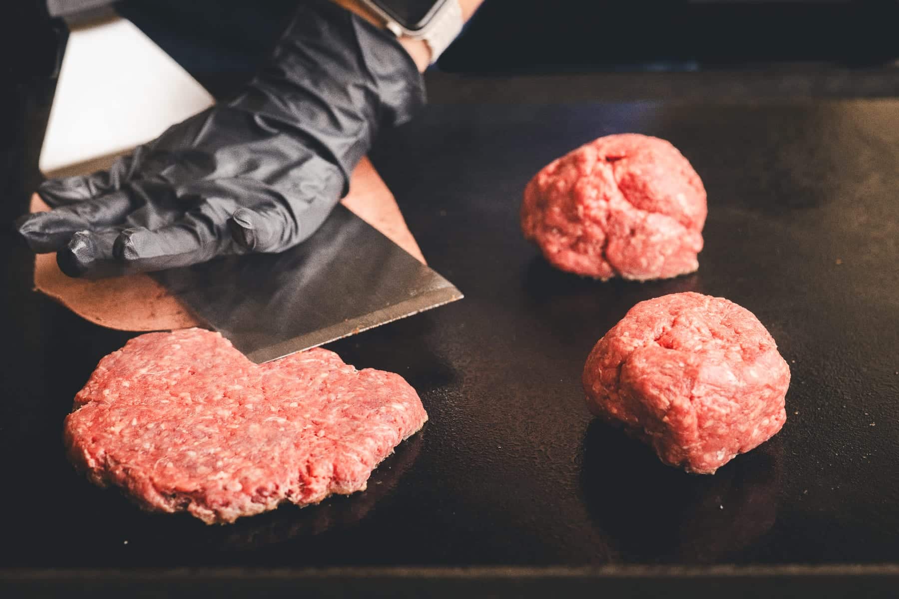 Ground beef patties being formed on cutting board with metal spatula.