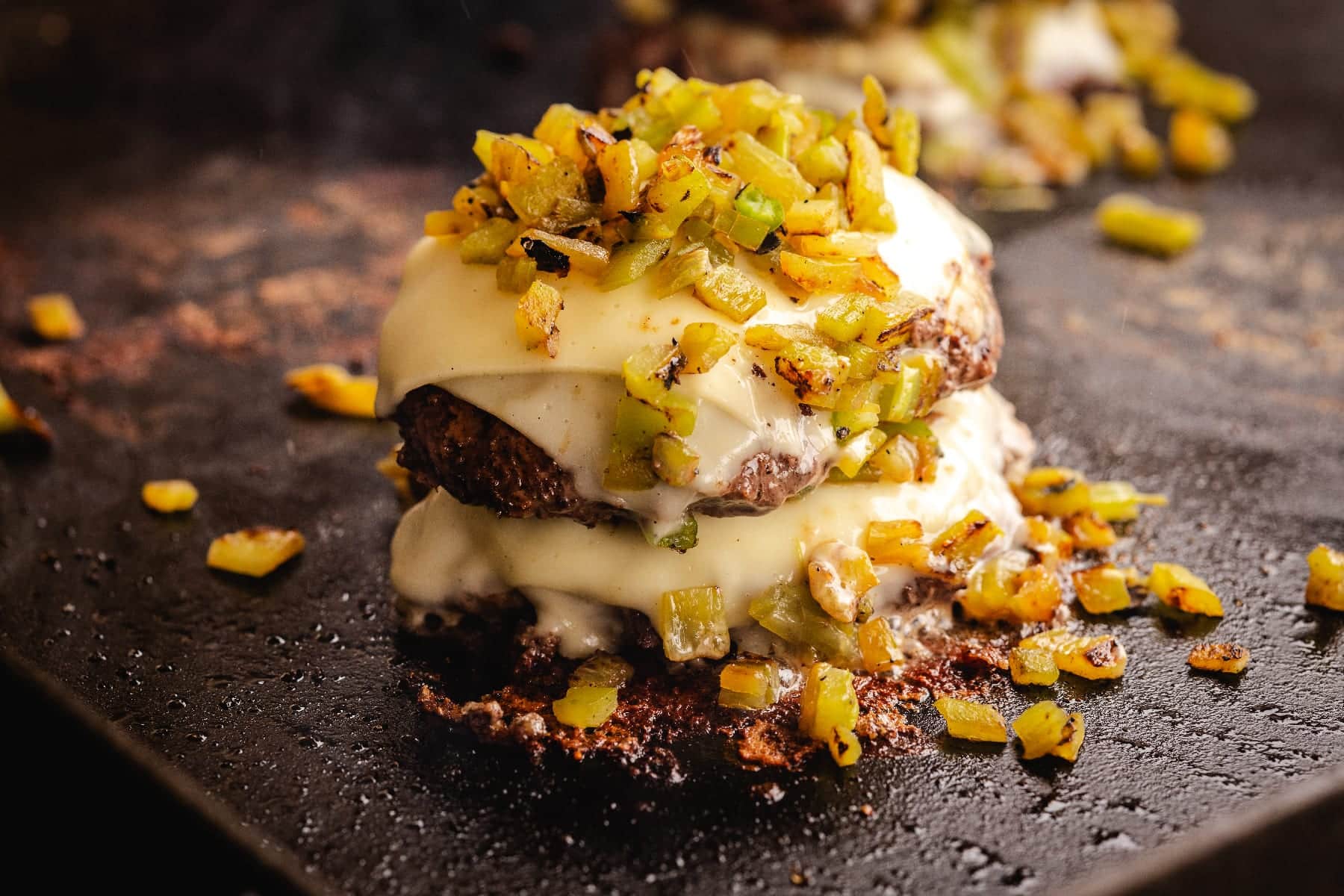 Double stacked patties with melted cheese topped with diced Hatch chiles on griddle.