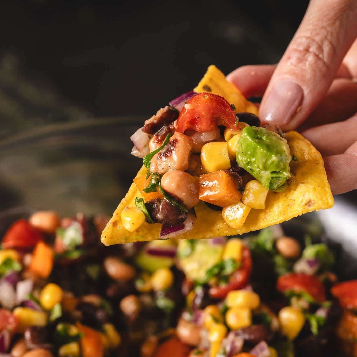 Tortilla chip dipped into cowboy caviar in glass bowl.