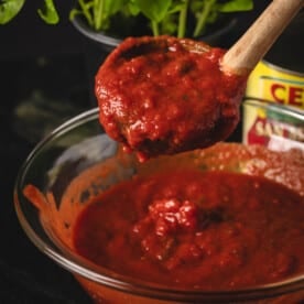 Wooden spoon scooping 4 ingredient pizza sauce from glass bowl.