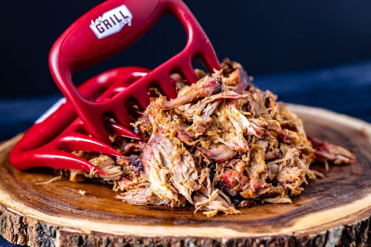 Smoked pulled pork with meat claws on wooden cutting board.