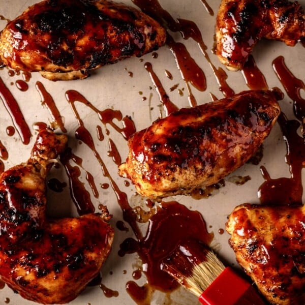 Chicken on baking sheet drizzled with BBQ sauce.