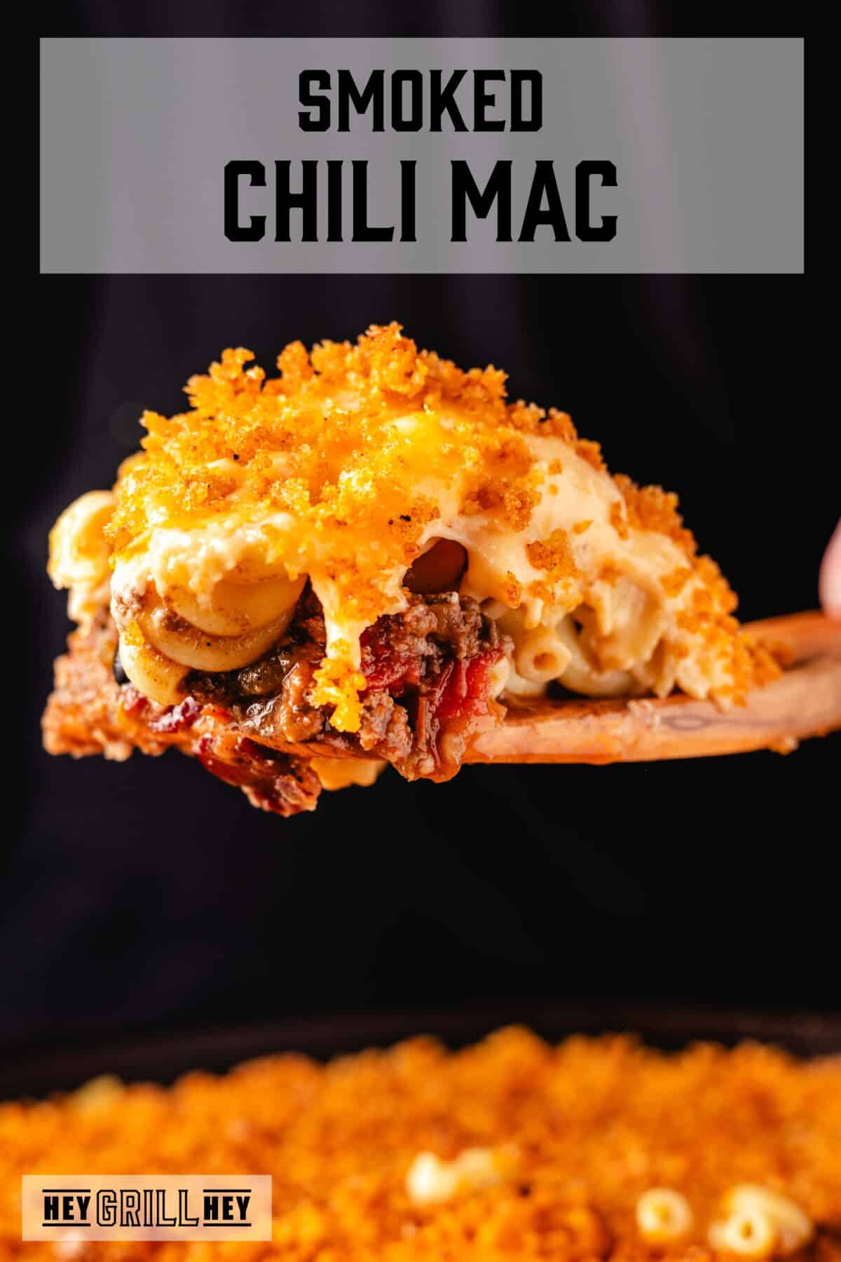 A scoop of chili Mac on a wooden spatula above a skillet. The text overlay reads "Smoked Chili Mac" at the top, and "Hey Grill Hey" at the bottom.