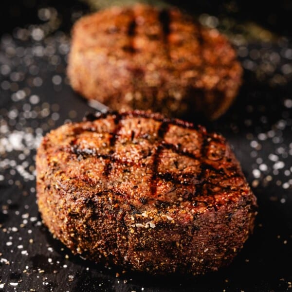 Grilled fillet mignon steaks on black cutting board with salt sprinkled on it.