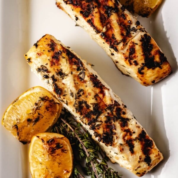 Grilled halibut on a white plate with lemon and thyme.