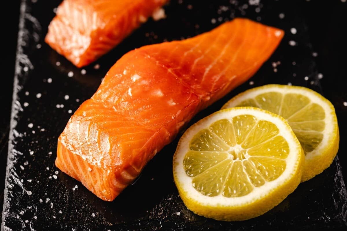Slices of salmon fillet on a black plate with lemon slices.