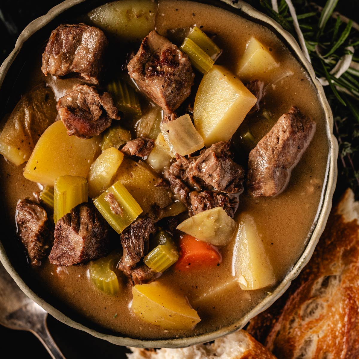 Beef stew in bowl next to bread.