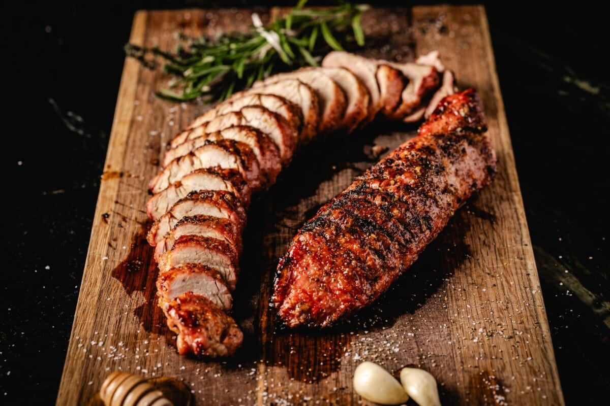 Sliced pork on cutting board with garlic cloves and honey.