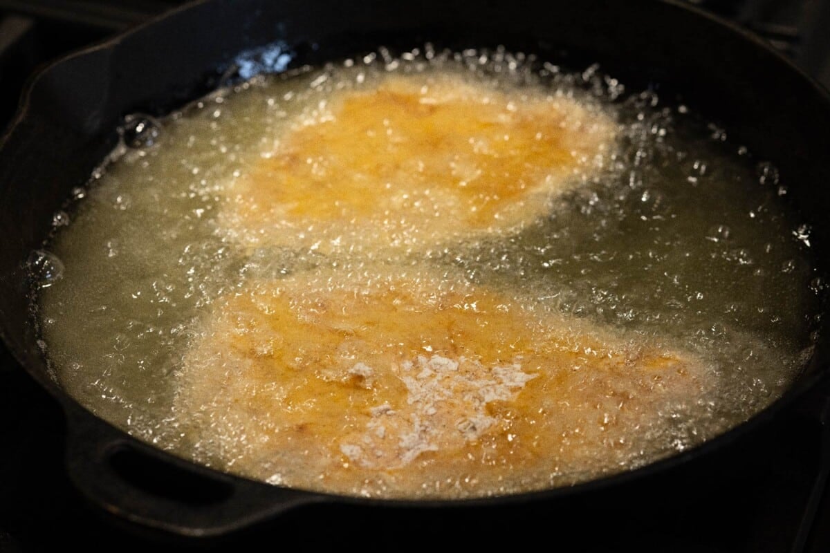Skillet with frying oil and breaded patties.