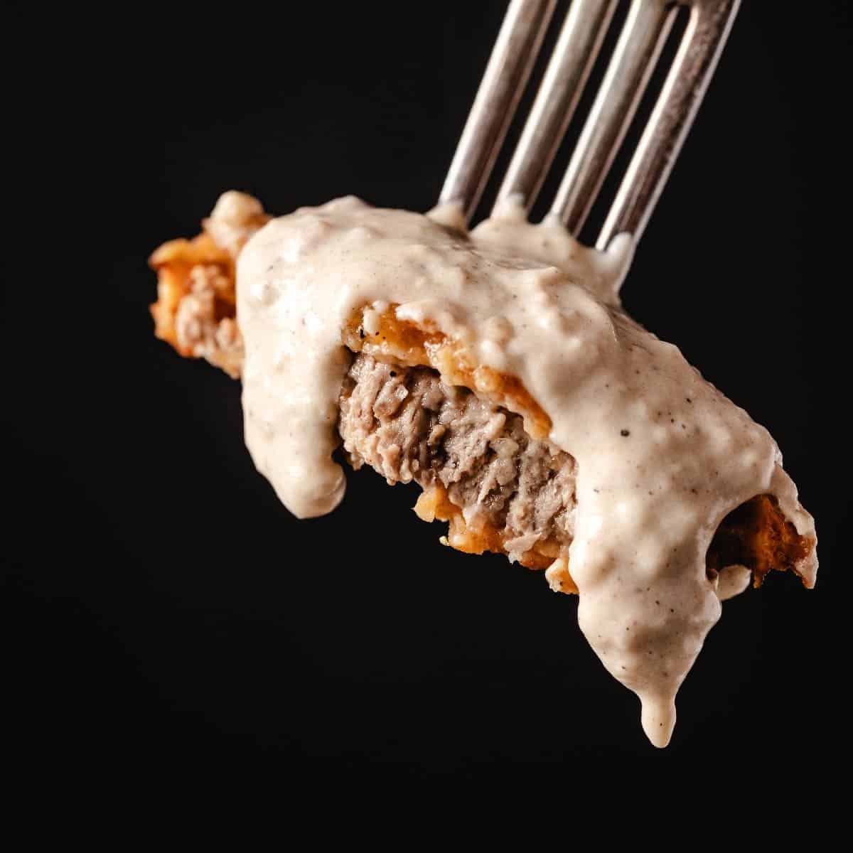 Chicken fried steak coated with gravy on fork.