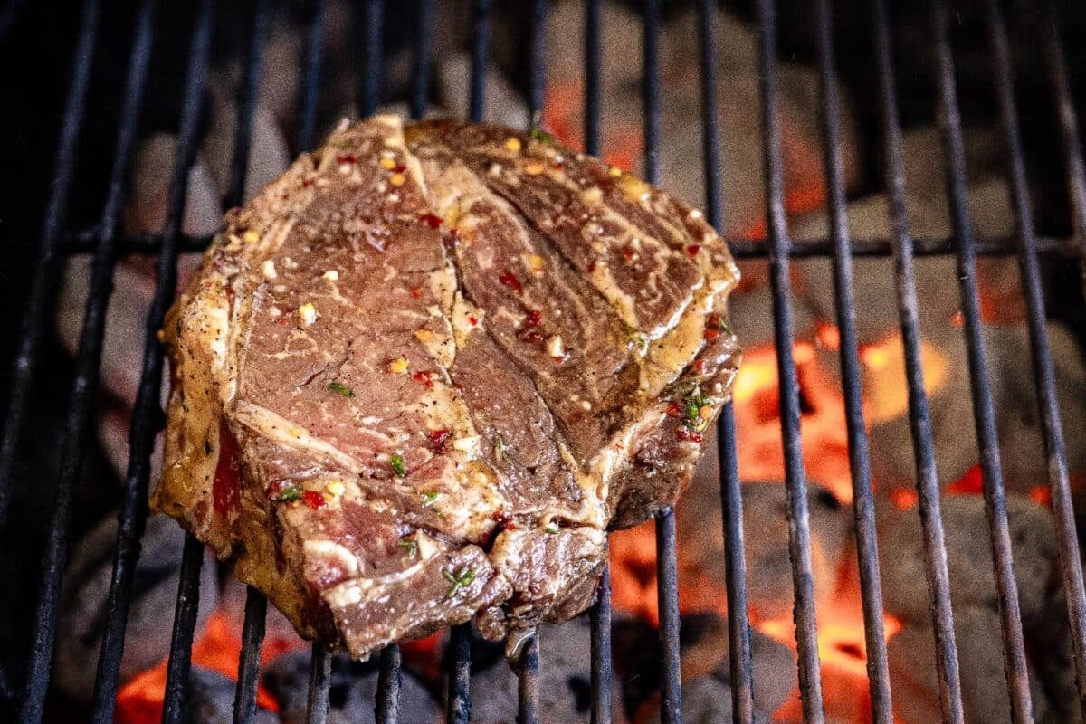 Delmonico steak on grill grates over charcoal.