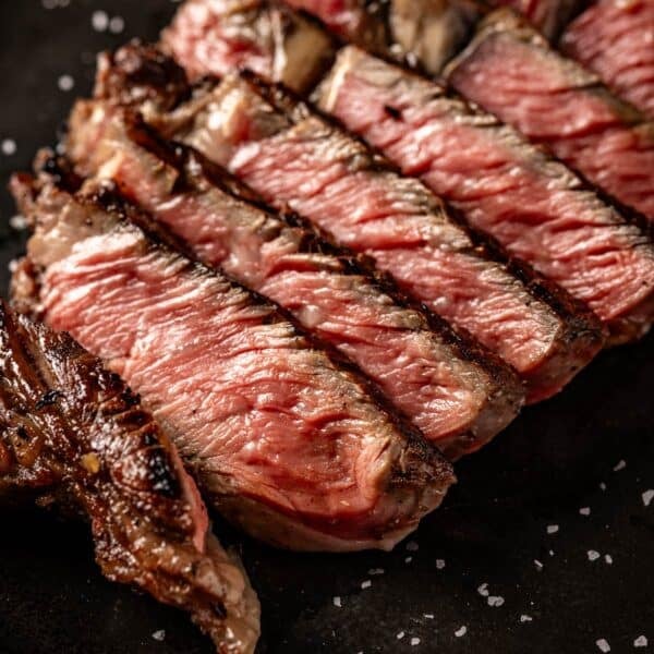 Sliced Delmonico steak on black serving platter.