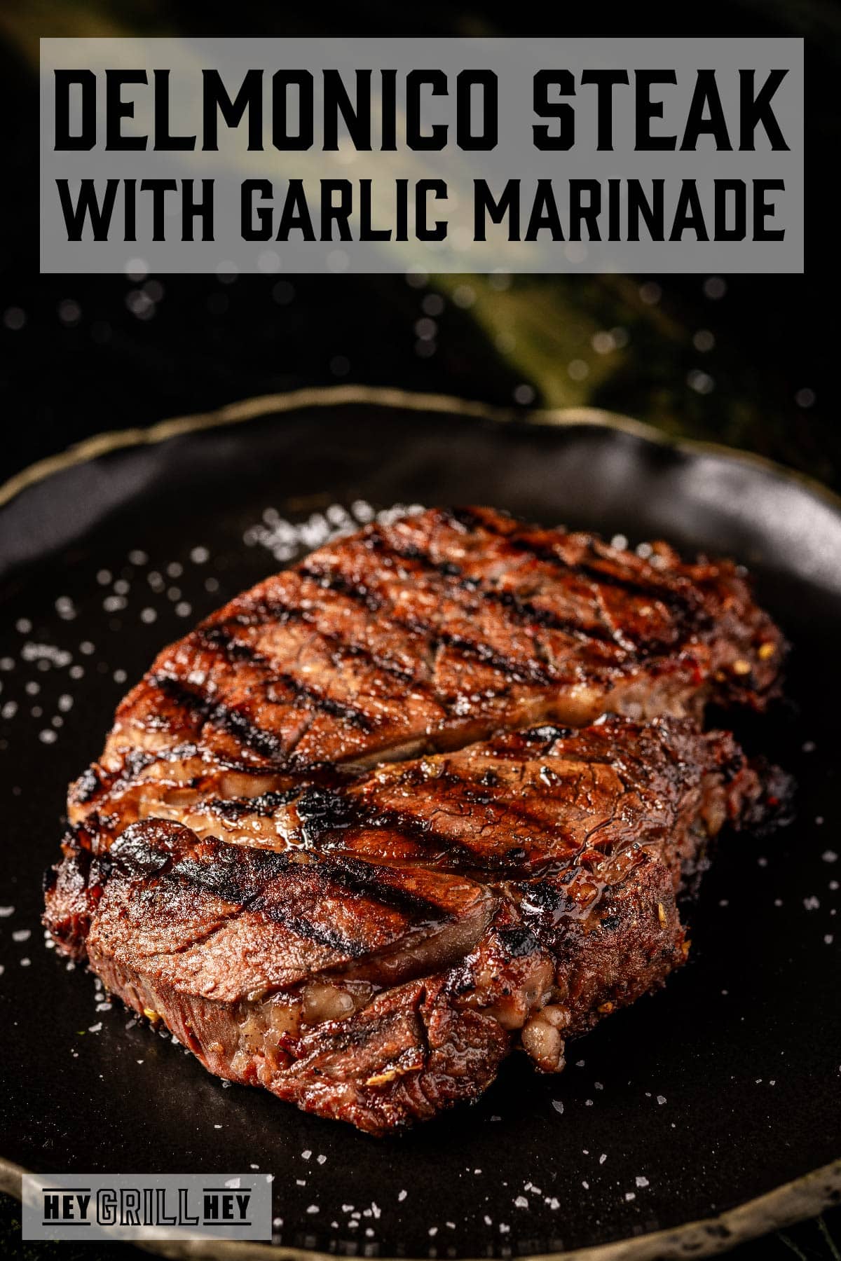 Seared steak on black plate. Text reads "Delmonico Steak with Garlic Marinade".