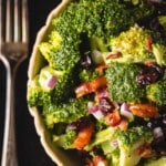 Broccoli salad in white bowl next to fork.