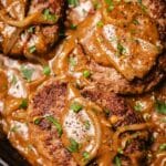 Hamburger steaks in onion gravy in cast iron skillet.