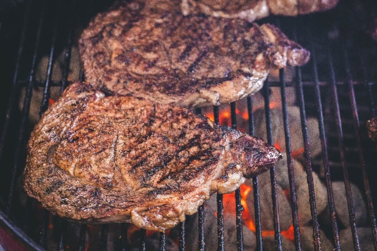 Ribeye steaks on grill grates over charcoals.